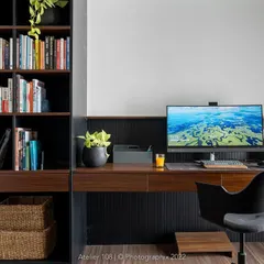 Home offices are trendier than ever. This sleek workspace features a dark wood desk with integrated shelving, providing ample storage and a sophisticated environment for productivity. The greenery adds a touch of life.