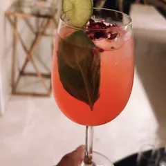 A beautifully crafted signature gin cocktail, showcasing our attention to detail. We use fresh ingredients like basil and rose petals, with a lime wheel garnish, to create drinks that are as visually appealing as they are delicious.