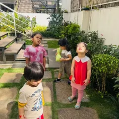 Children look up at the sky and around the garden, observing how the sun's position affects the shadows of trees and buildings. This is a simple, powerful lesson in earth science.