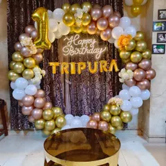 A premium first birthday setup for Tripura, featuring a full balloon ring in white, gold, and rose gold. The design includes a neon sign and a foil number '1' balloon.