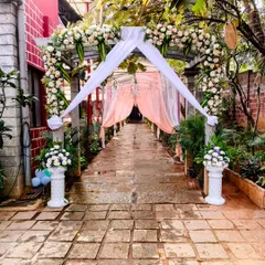 This charming garden entrance features a wooden archway covered in white flowers and greenery. Soft white and peach drapes add a touch of romance, creating a beautiful welcome for guests.