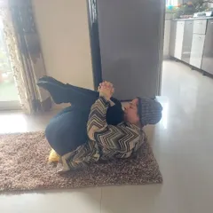 A senior client practices Pawanmuktasana (Wind-Relieving Pose) during a personal session at her home. This gentle pose is excellent for improving digestion and releasing tension in the lower back.