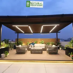A completed rooftop project in Gurgaon featuring a large pergola over a composite wood deck. This setup creates an ideal outdoor lounge, complete with comfortable wicker furniture, integrated planters, and modern linear LED lighting for a sophisticated evening atmosphere.