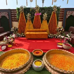 This traditional Haldi stage combines rich marigold garlands with elegant white floral arrangements. The setup includes large brass urlis filled with flower petals, ready for the ceremony.