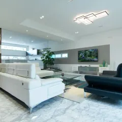 This expansive living room showcases modern minimalism with its marble flooring, clean white walls, and carefully selected furniture. A slatted wood partition provides a subtle visual separation without closing off the space, maintaining an open and airy feel.