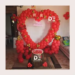 A romantic anniversary decoration for an at-home celebration, featuring a large heart-shaped balloon arch in red and gold.