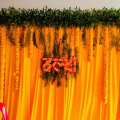 This is a classic and budget-friendly Haldi backdrop. It features a vibrant yellow drape, accented with hanging marigold strings and a custom sign made of flowers, creating the perfect festive photo spot.
