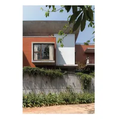 The facade of the Nairy Residence showcases a dialogue between materials. The warmth of exposed brick contrasts with the clean white plaster and the raw, board-formed concrete base, which is intentionally being overtaken by climbing plants to integrate the structure with its landscape over time.