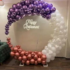 A sophisticated circular organic balloon arch in metallic purple, rose gold, and white for a retirement party. This modern design, complete with a "Happy Retirement" neon sign, honors a colleague's career in style.