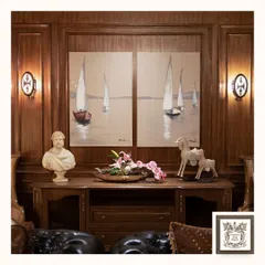 A pair of classic wall sconces flank a large seascape painting, adding symmetry and a touch of old-world charm to this elegant room. Their warm light enhances the rich wood paneling and creates a cozy, inviting atmosphere.