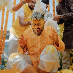 The groom braces himself as his friends pour jugs of milk over him during a joyous and messy Haldi in Thailand.