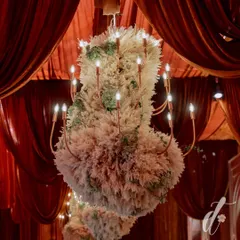 For this wedding, we designed custom chandeliers dressed in pampas grass and succulents, suspended from a ceiling of draped red velvet. This created a dramatic, textural contrast and a truly unique lighting feature.