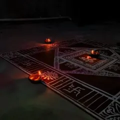 The Mandana design is almost complete, with geometric borders and floral patterns surrounding the central square. A single diya is lit, giving a first hint of the beautiful glow to come.
