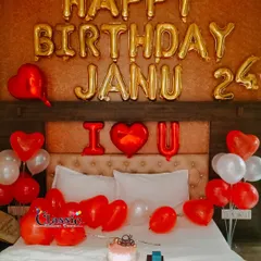 A romantic birthday bedroom decoration with red and white heart-shaped balloons, foil letters, and a cake ready for celebration.
