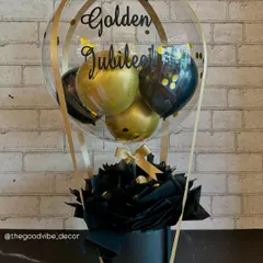 A sophisticated Bobo Box we designed for a Golden Jubilee celebration. This arrangement features a black base with black and gold balloons, confetti, and a custom "Happy Golden Jubilee" message in elegant script.