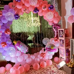 A clear shot of the 'Welcome Baby' ring backdrop, decorated with pink and purple balloons, baby-themed foil balloons, and a 'WELCOME' message made of rose petals.