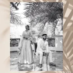 A classic black and white portrait with a high-fashion edge. The artistic framing with palm leaves and the couple's regal pose create a sophisticated and timeless image.