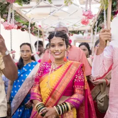 The radiant Maharashtrian bride makes her entrance, walking under a floral canopy held by her brothers, her smile filled with anticipation.