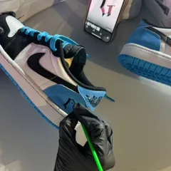 An artist carefully paints a custom initial onto a pair of Air Jordans. We use reference images on our phones to ensure every detail, like this gothic font, is perfectly executed.