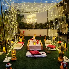 An intimate birthday picnic under a canopy of fairy lights. This square frame creates a "room" of light around the low table and cushions, making the garden setting feel extra special and enclosed.