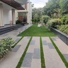 A modern walkway design for an urban residence, using large stone pavers interspersed with strips of green lawn. This hardscaping technique breaks up the solid surface, allowing for better water drainage and integrating greenery into the pathway itself.