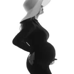 An elegant and artistic high-contrast silhouette. The mom-to-be wears a stylish hat, creating a chic and mysterious portrait that focuses entirely on her beautiful form.