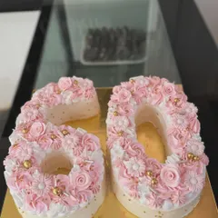 A close-up of the beautiful "60" monogram cake, showing the detailed piping work of the buttercream flowers and the delicate gold bead accents.