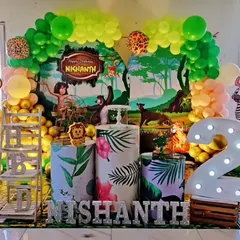 A Jungle Book themed birthday party for a second birthday. This decoration includes a forest backdrop, character cutouts of Mowgli and Baloo, and a large marquee number '2'.