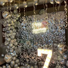 A glamorous 7th-anniversary celebration with a silver sequin shimmer wall. I framed it with a silver chrome balloon arch, added butterfly details, and hung more balloons from the ceiling to create a sparkling, festive atmosphere.