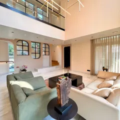 In this Gurugram villa, we designed the living area to be a grand yet inviting double-height space. The focus was on creating a warm, luxurious atmosphere for family gatherings, using a palette of soft tones, natural light, and a statement chandelier that acts as a sculptural centerpiece.