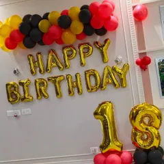 Celebrating an 18th birthday with a bold color scheme. This wall decoration uses red, yellow, and black balloons with large gold foil letters and numbers to mark the special occasion.