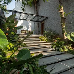A view of the entrance pathway, where floating concrete steps are surrounded by lush tropical foliage, leading up to the main door under a glass canopy.