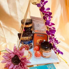 A modern and artistic take on Diwali gifting. This hamper features a unique triangular stand adorned with orchids, holding a curated selection of teas, chocolates, and festive sweets.