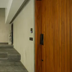 The clean lines of a vertically slatted wood door stand in warm contrast to the cool, textured finish of the surrounding concrete walls and stone steps. This image captures our focus on material honesty and precise detailing.