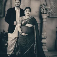 A formal couple's portrait in black and white, emphasizing their proud stance and traditional clothing. The lack of color adds a sense of history and permanence to this Maharashtrian-themed maternity photo.