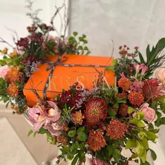 I love matching the floral design to the gift itself. Here, a luxury gift box is enveloped in a rich, autumnal palette of pincushion proteas, cymbidium orchids, and deep red chrysanthemums, creating a cohesive and artistic presentation.