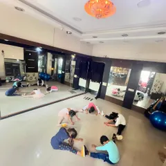 A wider view of the kids' dance class doing their warm-up stretches in a circle, with their reflections in the studio mirror.