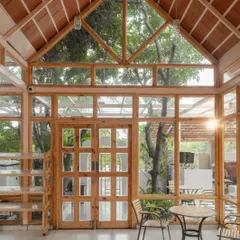The interior of the Bake House is a light-filled glass box with a pitched roof and exposed wooden framing. The transparency connects diners to the surrounding garden.
