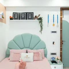 A close-up of the beautiful shell-shaped headboard in a mint green fabric, complemented by pink and white "Princess" cushions. The floating nightstand keeps the look clean and modern.