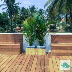 Here, I used beautiful, warm-toned wooden planks for the flooring and matching custom-built benches. The clean lines of the wood contrast nicely with the central planter box, which is filled with white pebbles and vibrant green plants, showcasing a modern and minimalist aesthetic.