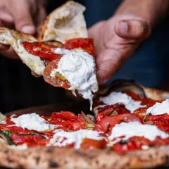 A perfect slice being lifted, showcasing the melted cheese and soft, airy crust. This pizza is topped with roasted peppers and dollops of fresh ricotta.