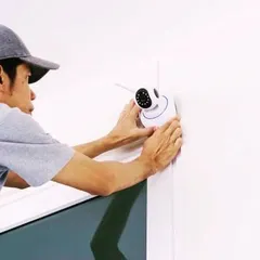 One of our technicians installing a compact indoor Wi-Fi camera. We ensure every device is positioned for optimal coverage and securely mounted for reliable operation.