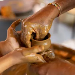 A beautiful, tactile shot of hands covered in wet clay, carefully molding a pot. This image captures the essence of our hands-on, therapeutic pottery experience.