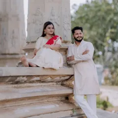 A relaxed portrait of the couple seated on ancient stone pillars in Melukote. This image showcases a blend of posed and natural moments during a pre-wedding or maternity shoot.