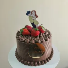 A decadent chocolate birthday cake topped with fresh strawberries and a cute couple topper.