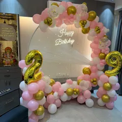 A lovely pink, white, and gold balloon ring for a 29th birthday. The setup includes large foil number balloons and a "Happy Birthday" neon sign.
