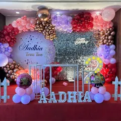 A grand second birthday celebration on a stage. This setup features a massive balloon garland in shades of pink and rose gold, a personalized circular backdrop, a sequin wall, and a light-up number '2'.