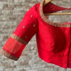 The quintessential red saree blouse. This piece is crafted from raw silk and features delicate gold embroidery along the neckline and a sheer panel on the sleeve.