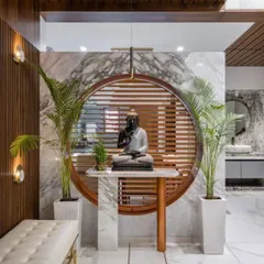 A peaceful meditation corner featuring a Buddha statue set against a circular wooden and marble backdrop. The design uses natural materials and plants to create a tranquil atmosphere.