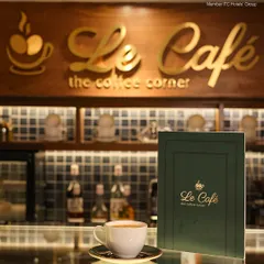 The counter at Le Cafe, with our elegant menu and a freshly brewed cup of coffee waiting for you. The golden logo in the background adds a touch of class to this cozy space.